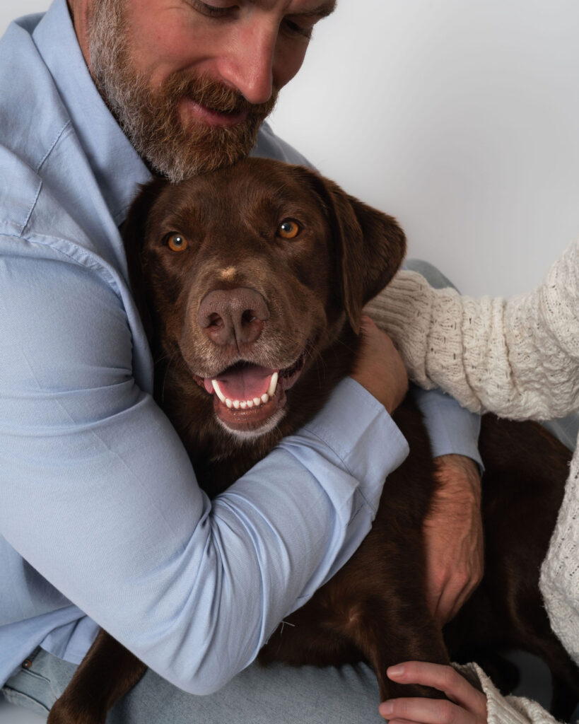 Man holding chocolate Labrador during family photos with dogs